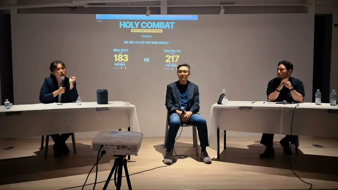 Three speakers on the Holy Combat New York stage, with the Holy Combat logo on screen